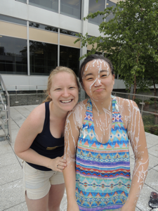 Two staff members together. On the left, the staff member is clean and happy! On the right, the other staff member is doused with Oobleck and is pouty.